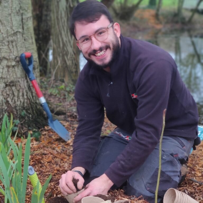 Gwenda Rouzic, Jeune paysagiste souriant en train de planter dans un massif au jardin, les mains dans la terre.